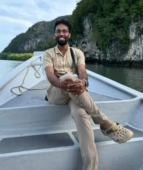 Uttham smiling on a boat, with green cliffs behind him